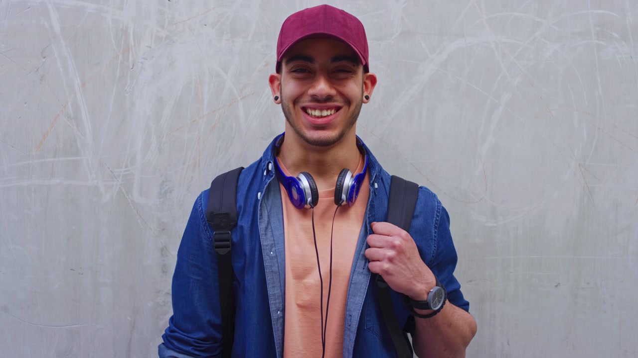 Smiling Young Man Wearing a Cap and Backpack Standing Against a Wall