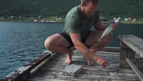 man removing gills from freshly caught mackerel fish on lakeshore