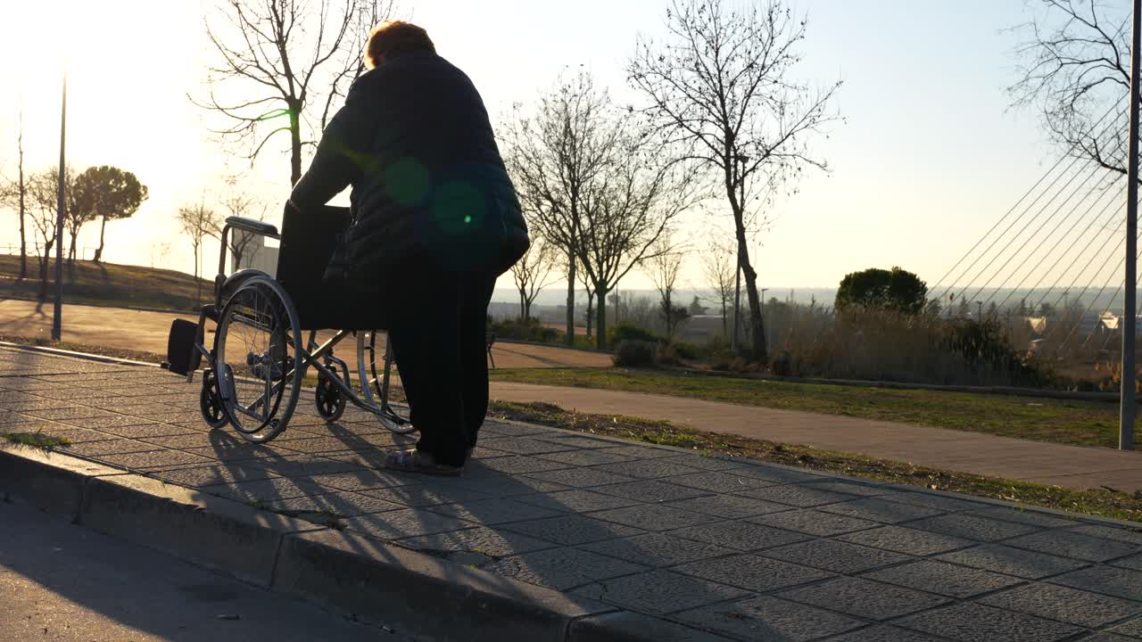 Granny walking with difficulty pushing the wheelchair in the park