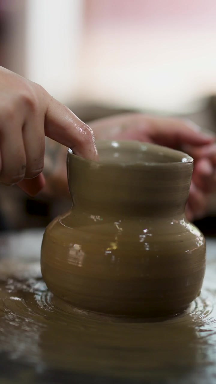 Primo piano di mani che modellano argilla umida in un vaso su un tornio da vasaio in rotazione