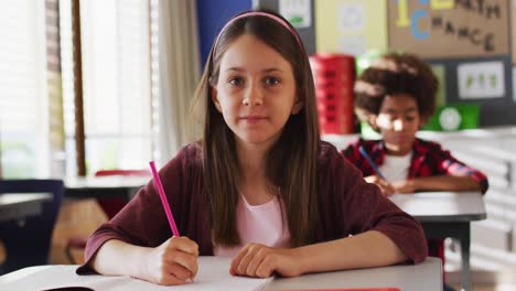 Portrait-of-caucasian-schoolgirl-sitting-in-class,-making-notes,-looking-at-camera