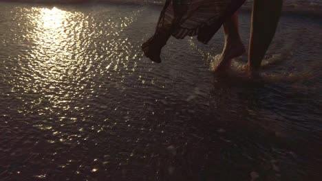 close up footage of a barefoot woman walking in the water towards the sunset in the beach.