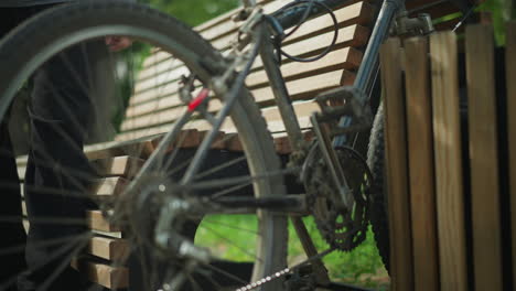 close-up of bicycle being moved into position between wooden bench and nearby structure in peaceful park, resting against bench while rider sits down to relax, surrounded by lush greenery