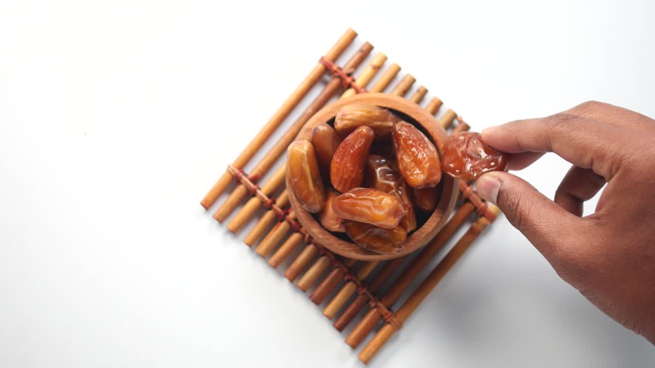 Hand Reaching for Dates in a Wooden Bowl