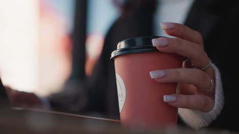 close-up of a woman's hand with manicured nails lightly tapping on a red juice cup lid while a blurred background reveals a professional setting