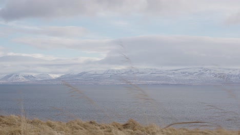 Icelandic-meadow,-lake-and-mountain-landscape-during-cloudy-and-windy-day