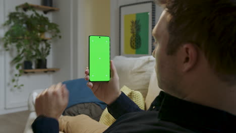 Man-holding-smartphone-in-his-hands-with-a-green-screen,-touching-the-screen-as-if-using-it