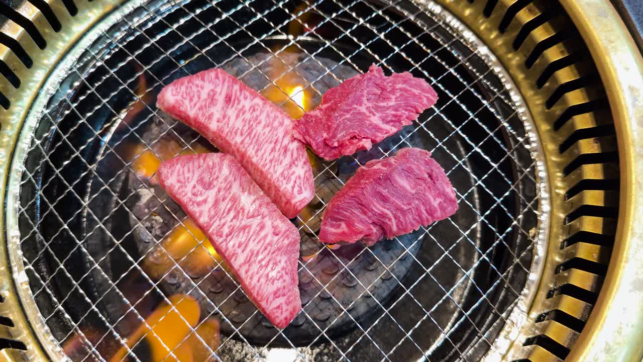 Ripresa dall'alto di manzo crudo marmorizzato che griglia su fiamme vive su un barbecue circolare a carbone.