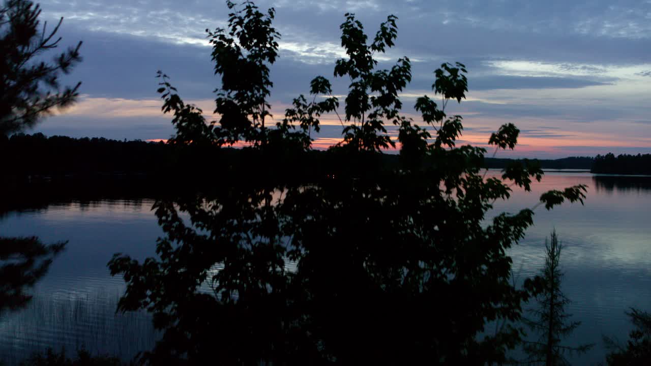 Aerial, drone flying over trees revealing lake at dawn dusk