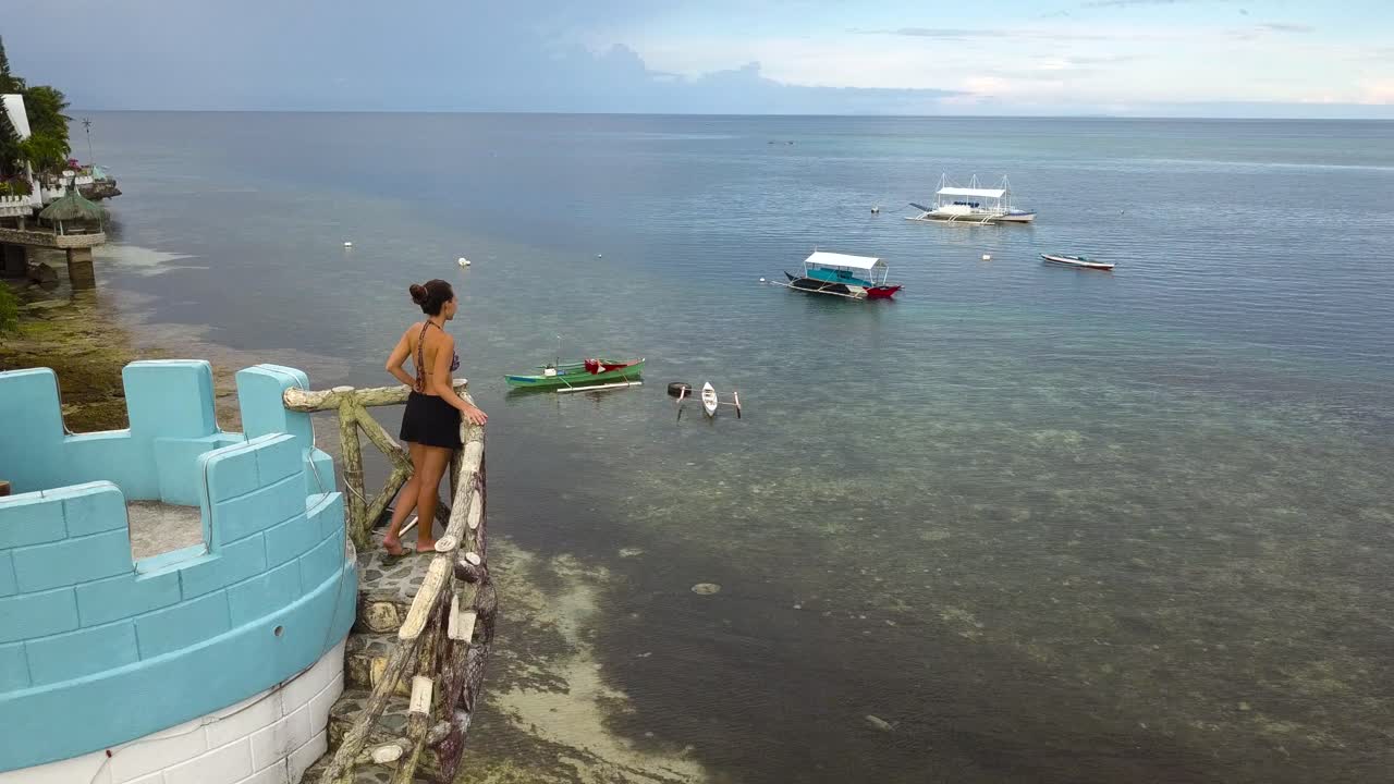 Woman looks out from tower over sea in Philippines, drone flies away