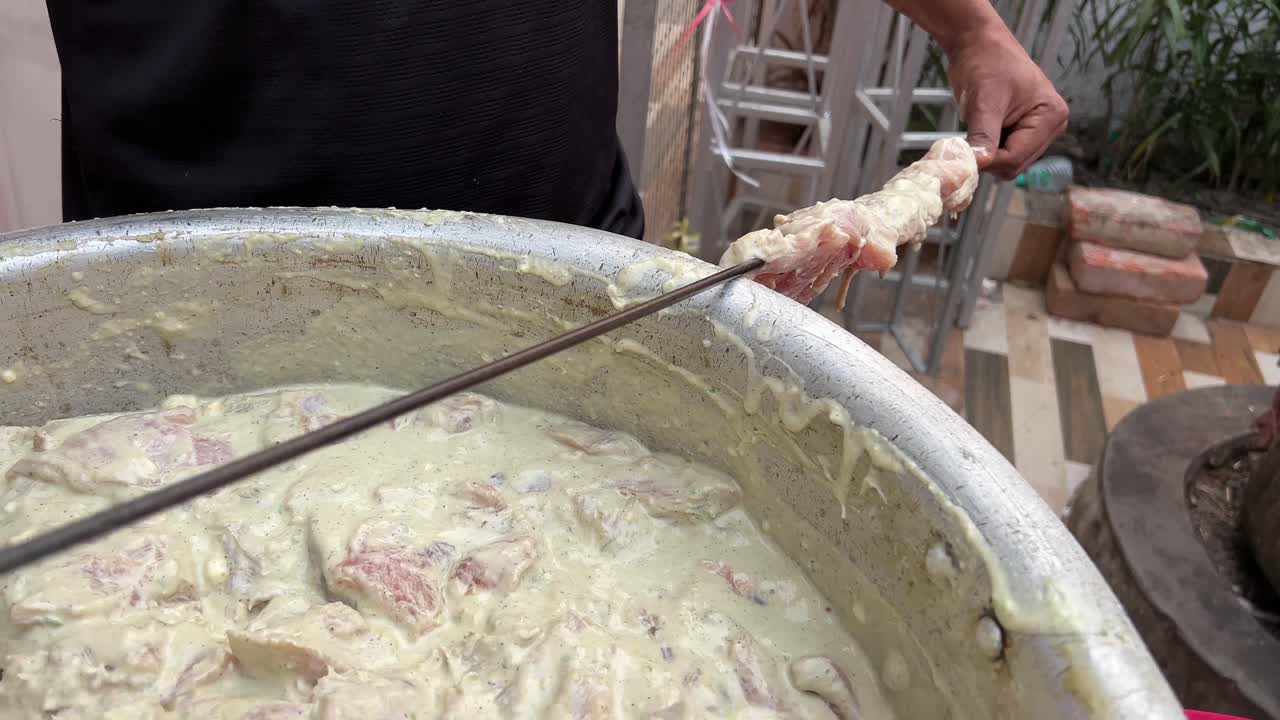 Male chef stringing raw chicken pieces in skewers for roasting.