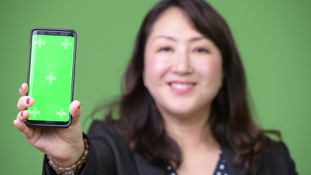 Mature beautiful Asian businesswoman showing phone