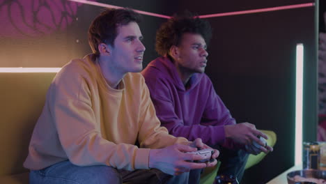 two concentrated friends playing video games sitting on sofa at home 1