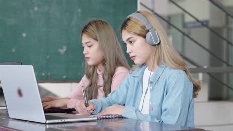 two asian girls student partners are working on a laptop help study together