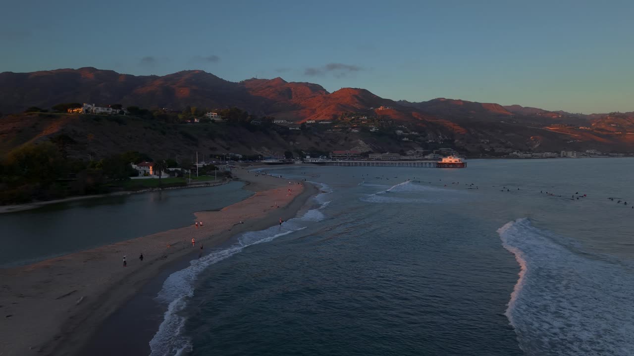 Onde al tramonto vicino al molo di Malibu, in California. Cavalcare le onde a Surfrider Beach e nella laguna di Malibu State Beach al crepuscolo serale. Gruppo affollato di persone che fanno surf sulla costa occidentale degli Stati Uniti.