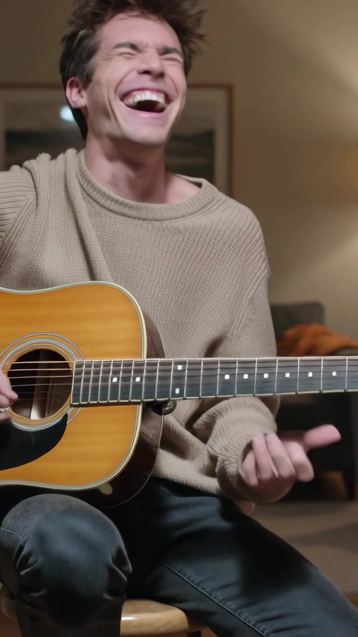 Video verticale: Uomo in maglione che strimpella e ride mentre suona la chitarra su uno sgabello dopo averla presa per divertimento.