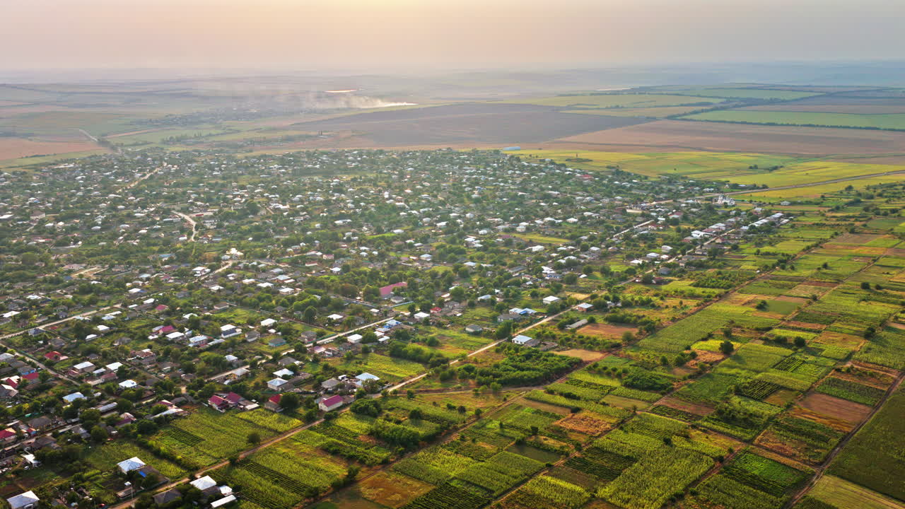 Aerial drone view showing a Moldovan village surrounded by vast farmlands and open fields under a hazy autumn sky