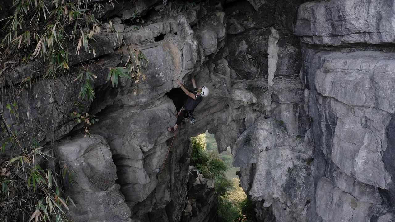 Rock climber ascending Treasure Cave in Yangshuo China, stone mountainside, aerial