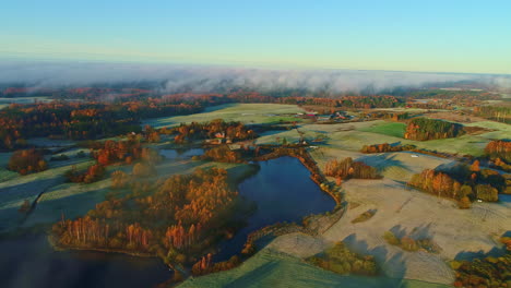 aerial flyover natural lake surrounded by autumnal forest landscape with fog and frozen grass