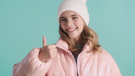 teenage caucasian girl with winter clothes and thumbs up in front of the camera.