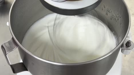 commercial heavy duty electric mixer mixing and whipping egg white until its peak, preparation for fluffy swiss meringue buttercream, close up shot