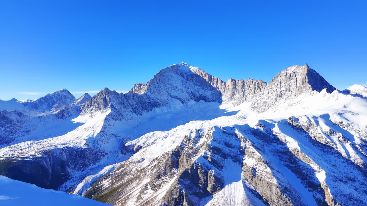 青空の下の雪をかぶった山頂、高山氷河とギザギザの尾根を捉えたパノラマ空撮ドローンショット。