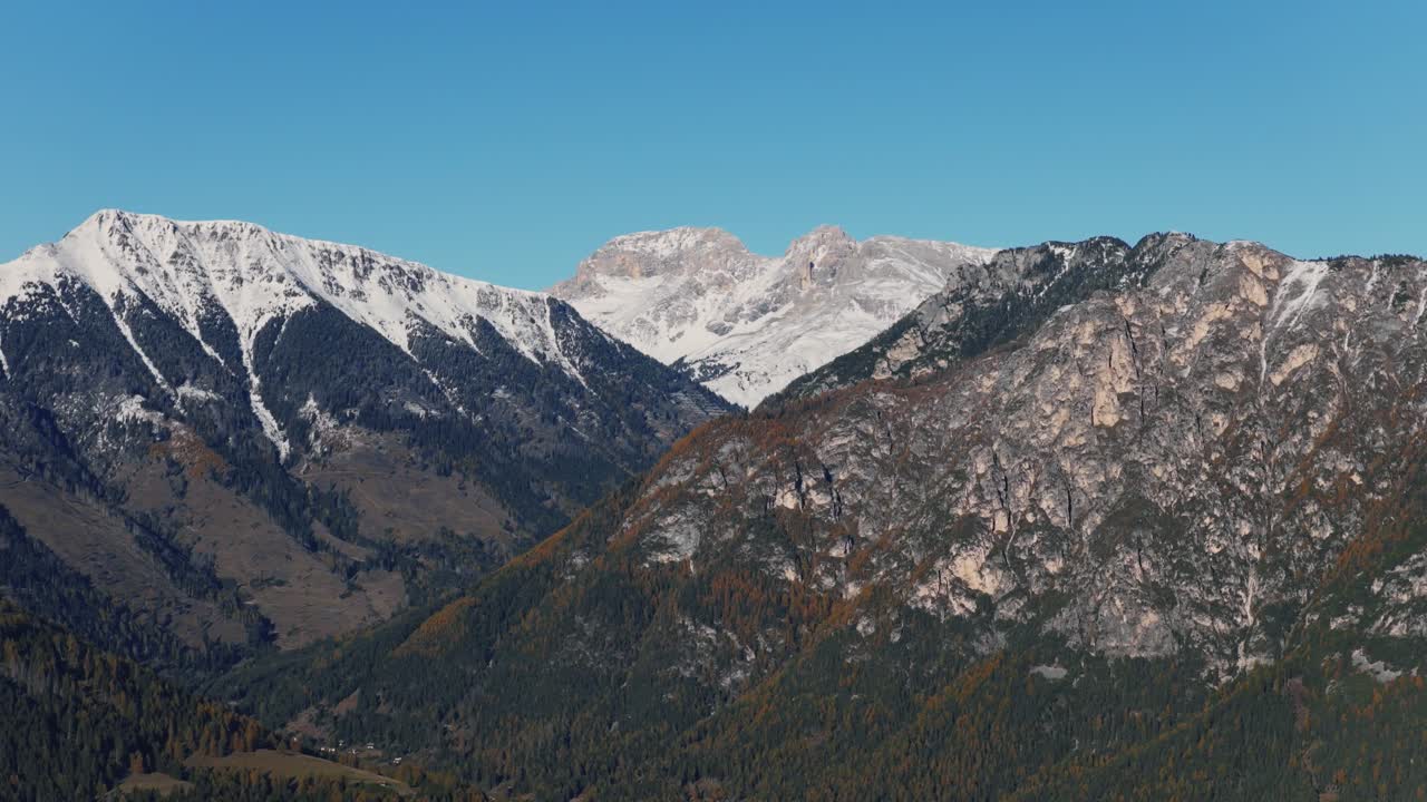 Schneebedeckte Berggipfel über zerklüfteten, bewaldeten Hängen im Val di Fiemme, Trentino, Italien. Weite Luftaufnahme