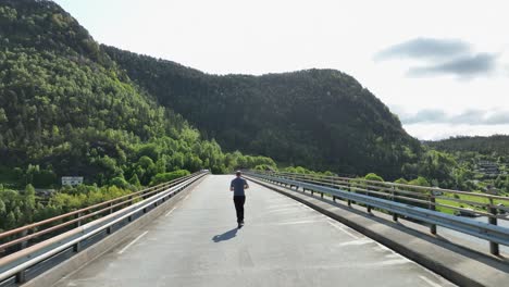 low aerial following man jogging on bridge over fjord in norway