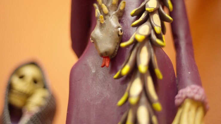 Closeup of handmade Catrina sculpture with moth decorations and floral hat, macro descend along dress and snake garment ornament