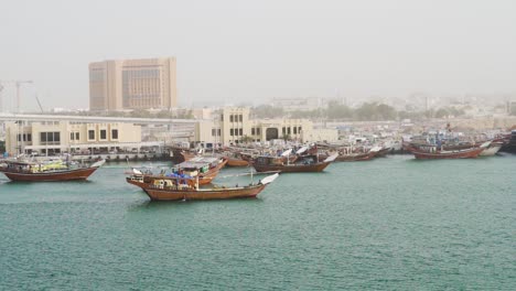 Traditionelle-Dau-boote-Segeln-Am-Dubai-Creek-Mit-Stadtgebäuden-Im-Hintergrund-In-Dubai,-Uae