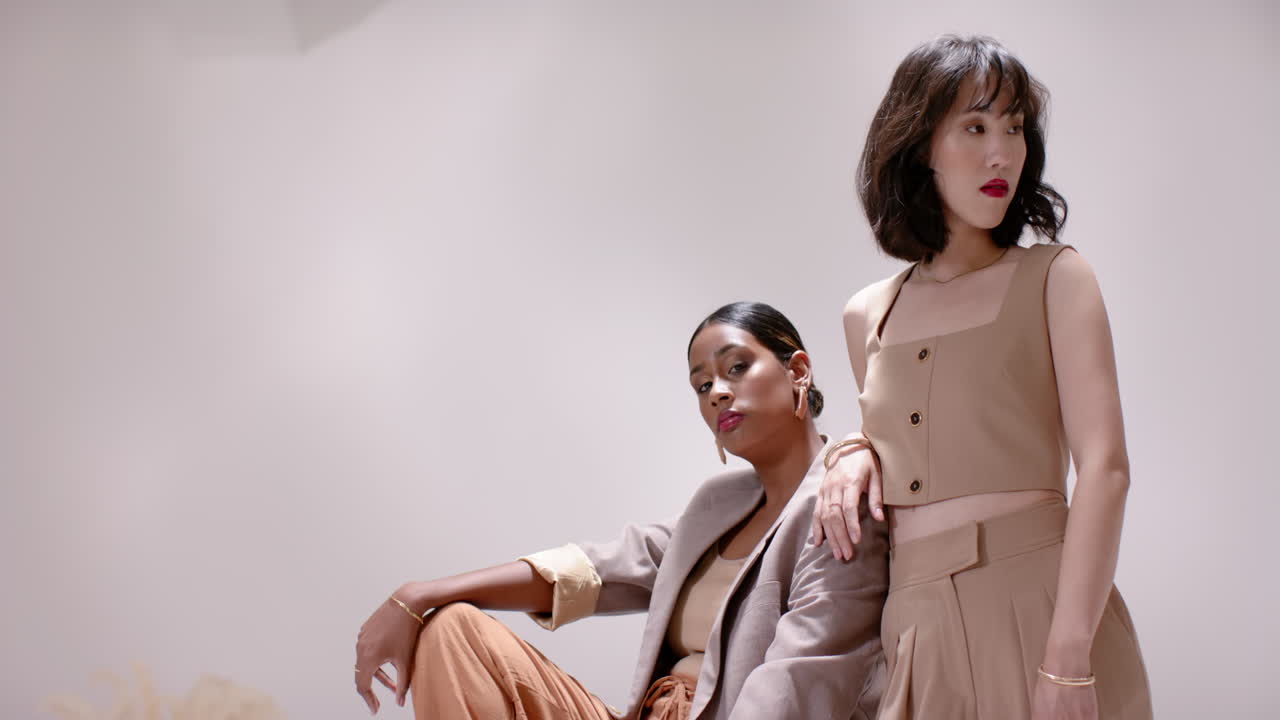 Shifting on cube, Indian and Chinese models adjusting blazer, posing for fashion shoot in studio