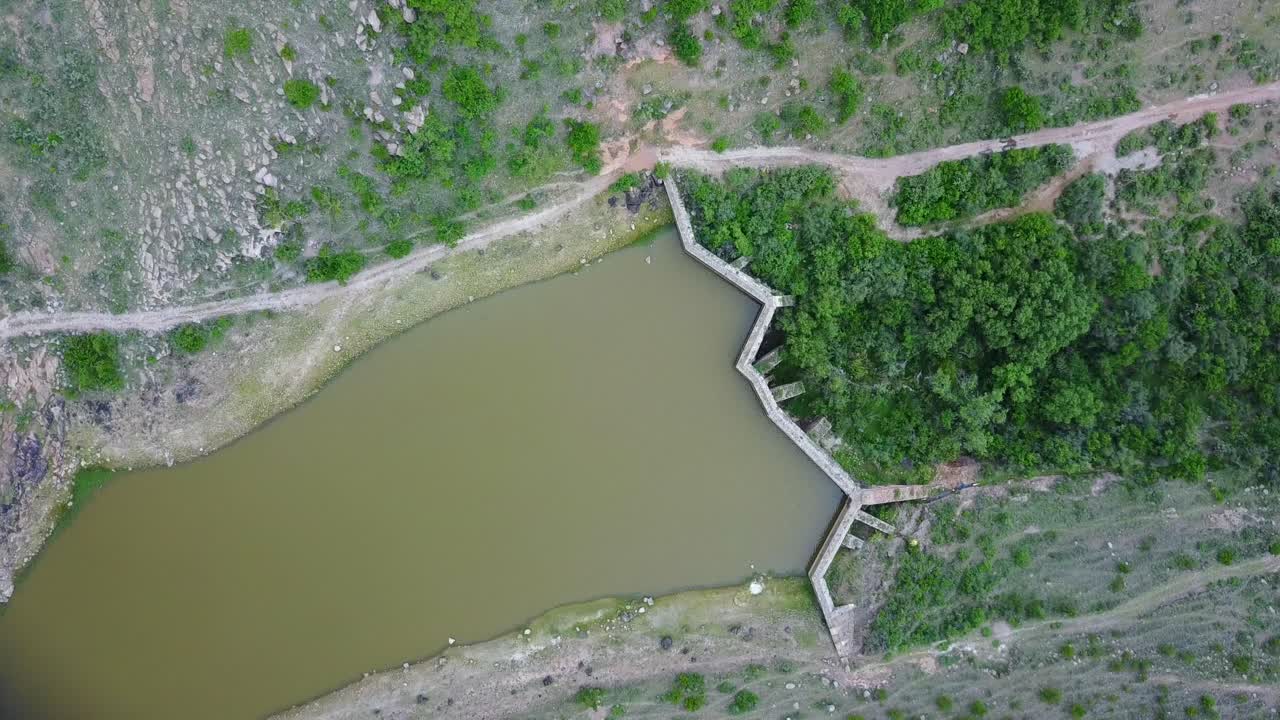 toma rotativa aérea de arriba hacia abajo de la presa marrón verde en un valle de montaña exuberante