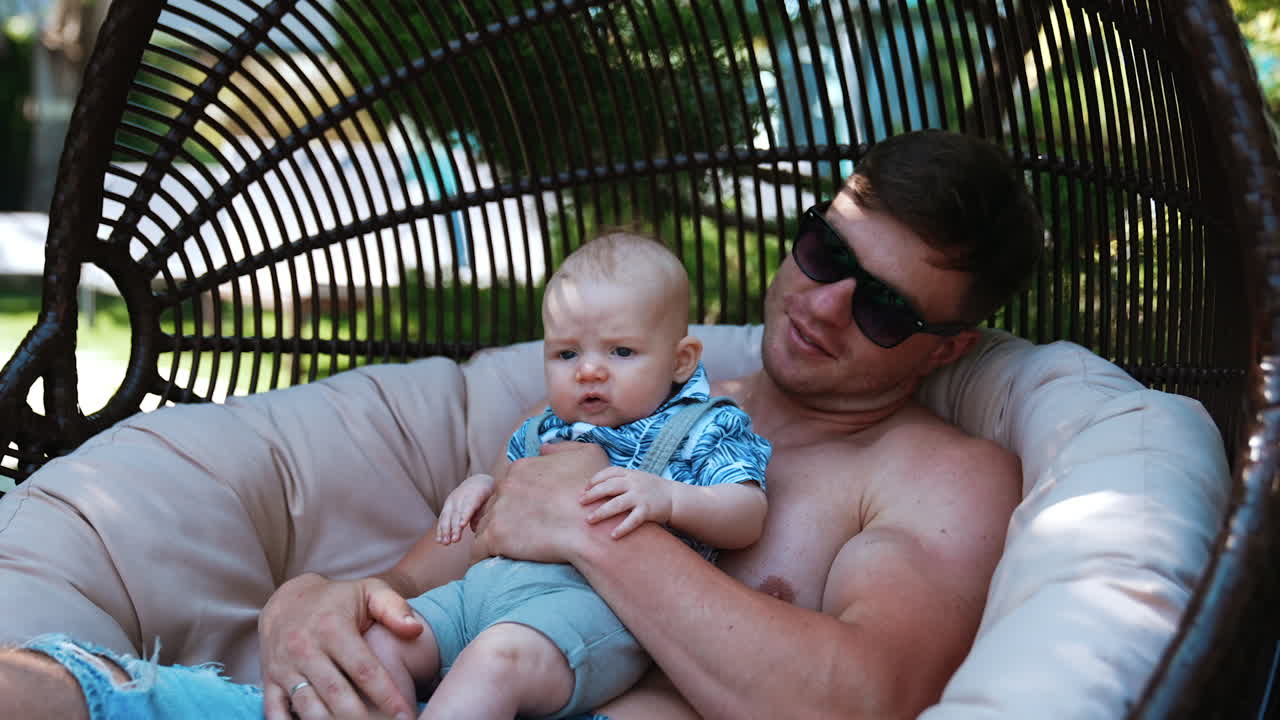 Dad holding his tiny baby son and kisses him on the head. Father having rest outdoors with his infant child.