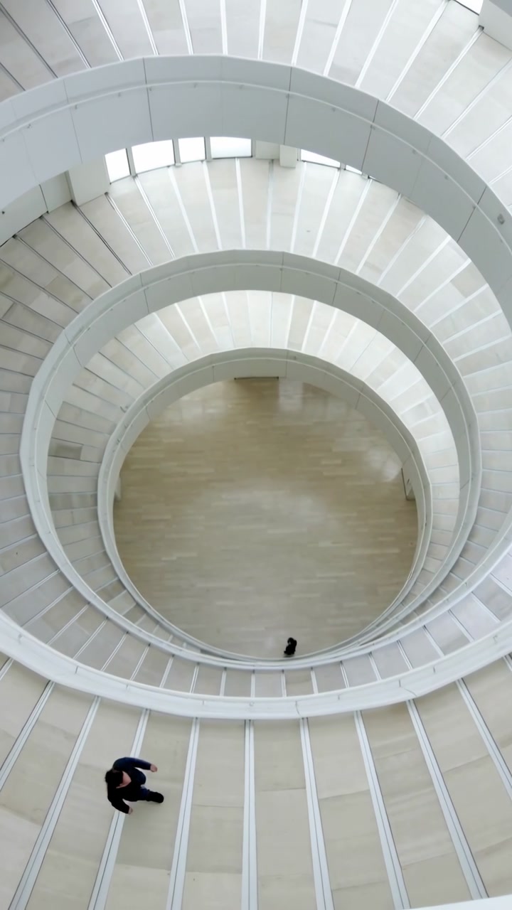 Vertical video: Starting with outer walker in dark coat going down spiral ramp in modern atrium