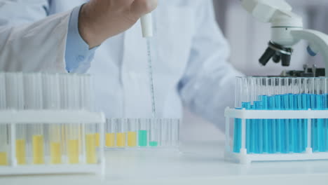 laboratory. hand in blue glove moves the tubes and drips blue liquid. medical worker holding yellow and blue liquid sample in test tube analyzing urine in lab. high quality 4k footage