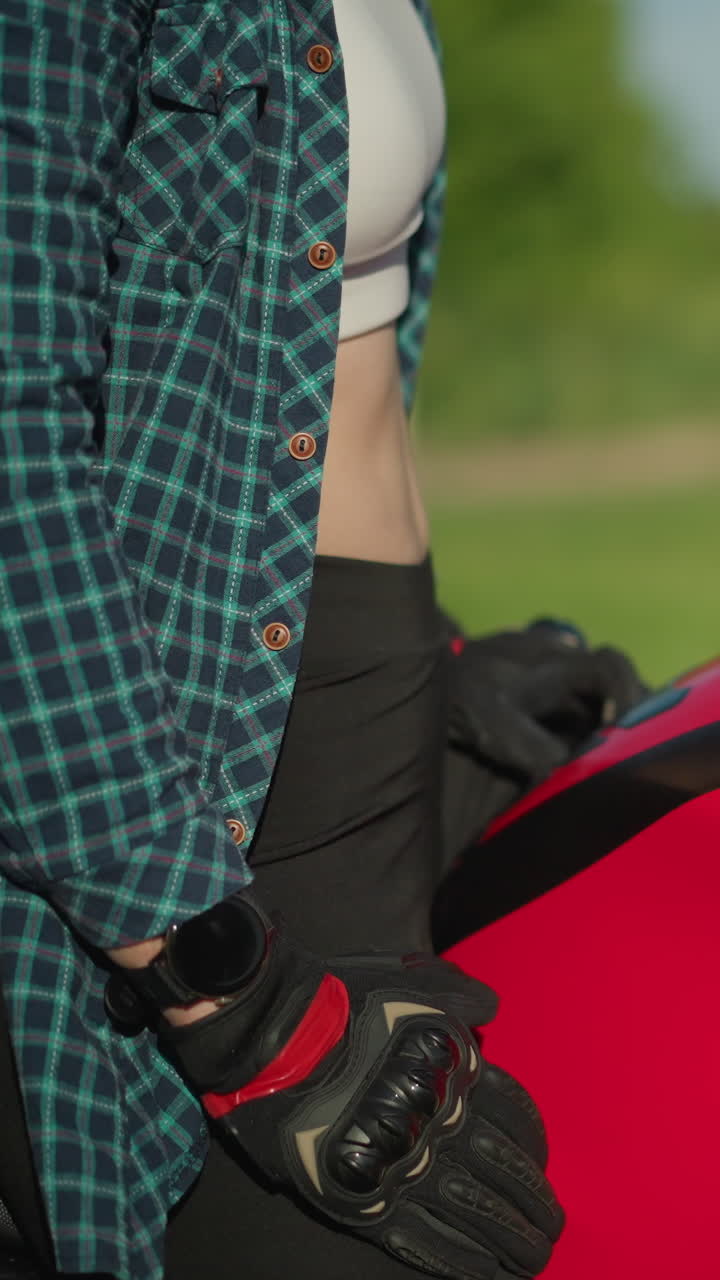 primer plano de una motociclista femenina descansando su mano en su regazo después de quitarla suavemente del tanque de su bicicleta roja, lleva guantes de protección negros