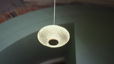 modern pendant light with intricate glass texture glows warmly while suspended from ceiling inside stylish space featuring soft green tones and exposed brick accents adding charm to ambient setting