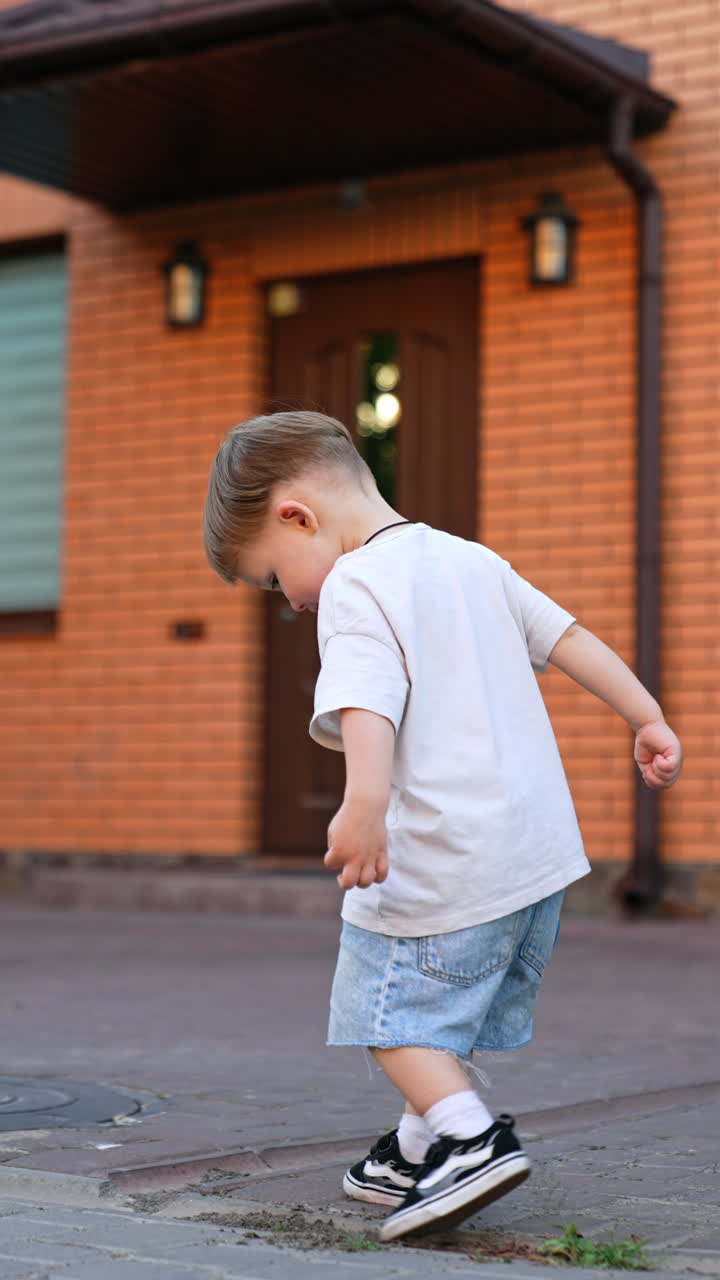 Kyiv, Ukraine, 25 May 2025: Young boy walking outside a modern home. A young boy explores the pavement in front of a brick house, showcasing his playful curiosity during the day