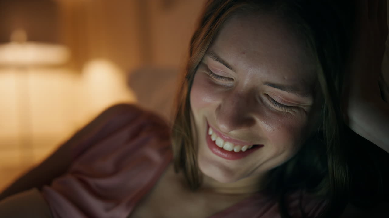 저녁 온라인 쇼를 가까이에서 보는 소녀. 스크린 빛에 웃는 웃는 얼굴