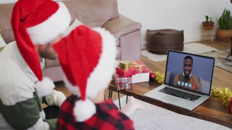 Caucasian-father-and-son-wearing-santa-hats-on-laptop-video-chat-during-christmas-at-home