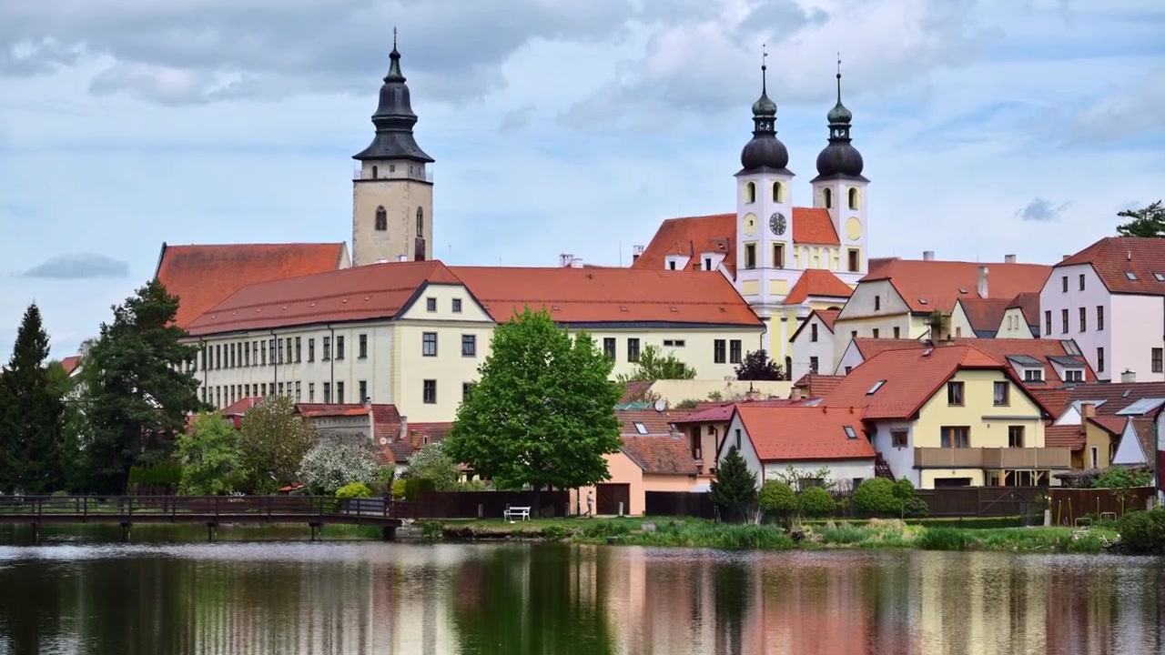 Udsigt til et renæssanceslot og tvillingekirketårne spejlet i en bydam, Telč, Tjekkiet