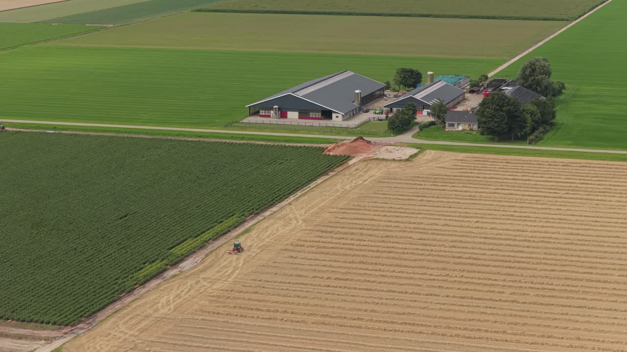 Luftfoto af traktor, der pløjer landlig landbrugsjord med gård i baggrunden, Holland