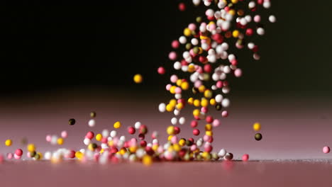 Sprinkles-pouring-onto-pink-surface-on-black-background