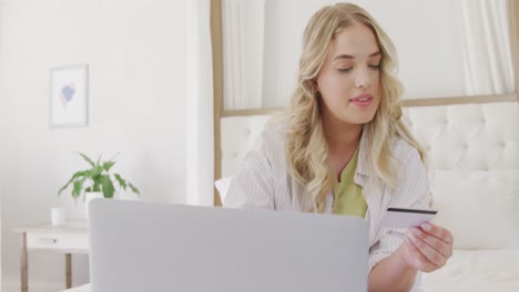 mujer caucásica feliz de talla grande usando una computadora portátil y sosteniendo una tarjeta de crédito en cámara lenta