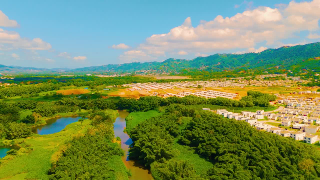 Drone footage of Gurabo River winding through lush trees beside community construction in Puerto Rico, filmed in late morning light. Perfect for real estate, environment, and infrastructure visuals