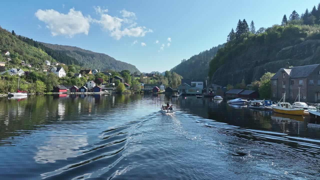 Drone footage of a boat with people sailing slowly in Hosanger toward cafe, surrounded by idyllic summer scenery, Norway