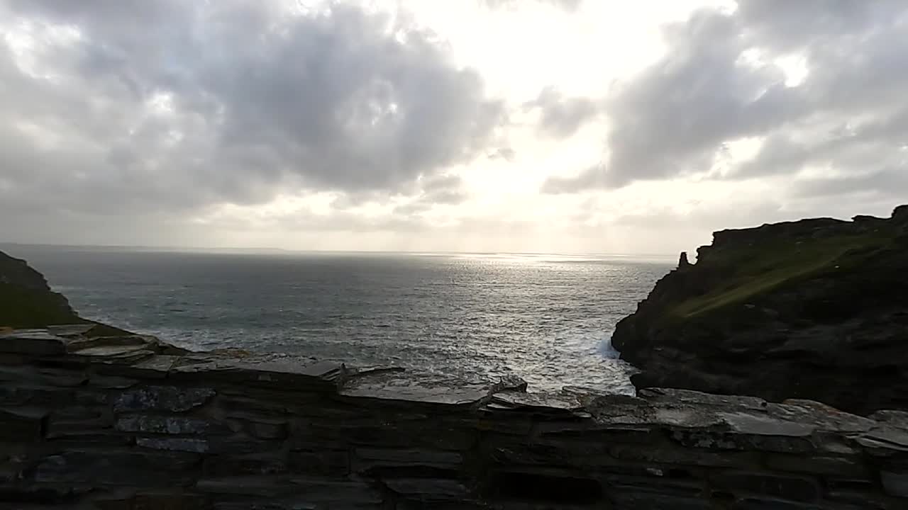 una vista de una puesta de sol sobre el océano desde detrás de una antigua ruina rústica de la pared en el castillo de tintagel del rey arturo