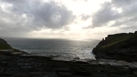 a view of a sunset over the ocean from behind a rustic, old wall ruin at king arthur's tintagel castle