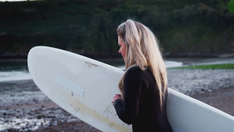 woman wearing wetsuit walking along beach into sea holding surfboard enjoying surfing vacation