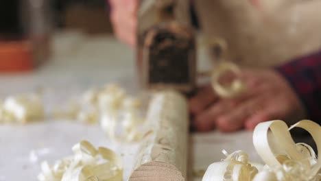 a macro shot of a carpenter using an antique traditional plane on a piece of wood in slow motion with a rack focus